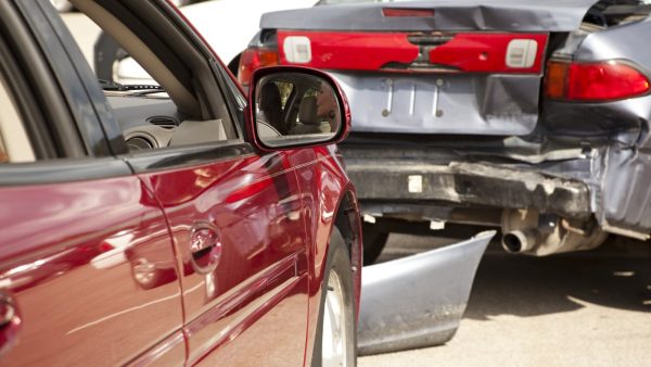 Close-up of a red car and a damaged silver car after a rear-end collision, showing visible bumper and body damage.