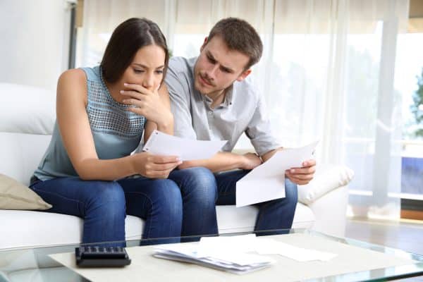 A worried couple sits on a couch reviewing paperwork.