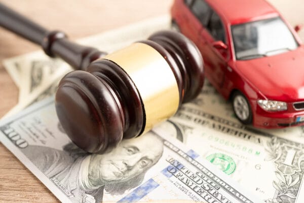 Close-up of a judge’s gavel resting on U.S. dollar bills beside a red toy car.