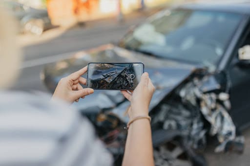 POV image of an individual using their smartphone to take a picture of their badly damaged car after an accident.